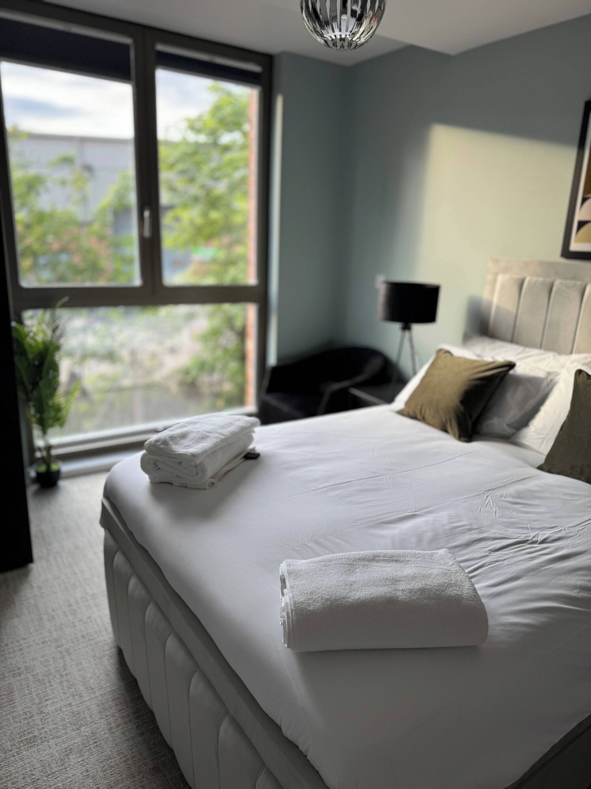 A bedroom with a large bed, a bedside lamp, and a view through a window.
