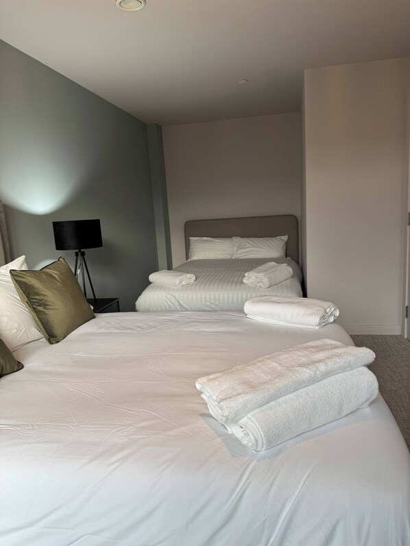 A hotel room with a large bed, a bedside lamp, and neatly folded towels. - Apartment in Botanical Gardens, Old Trafford (Manchester)