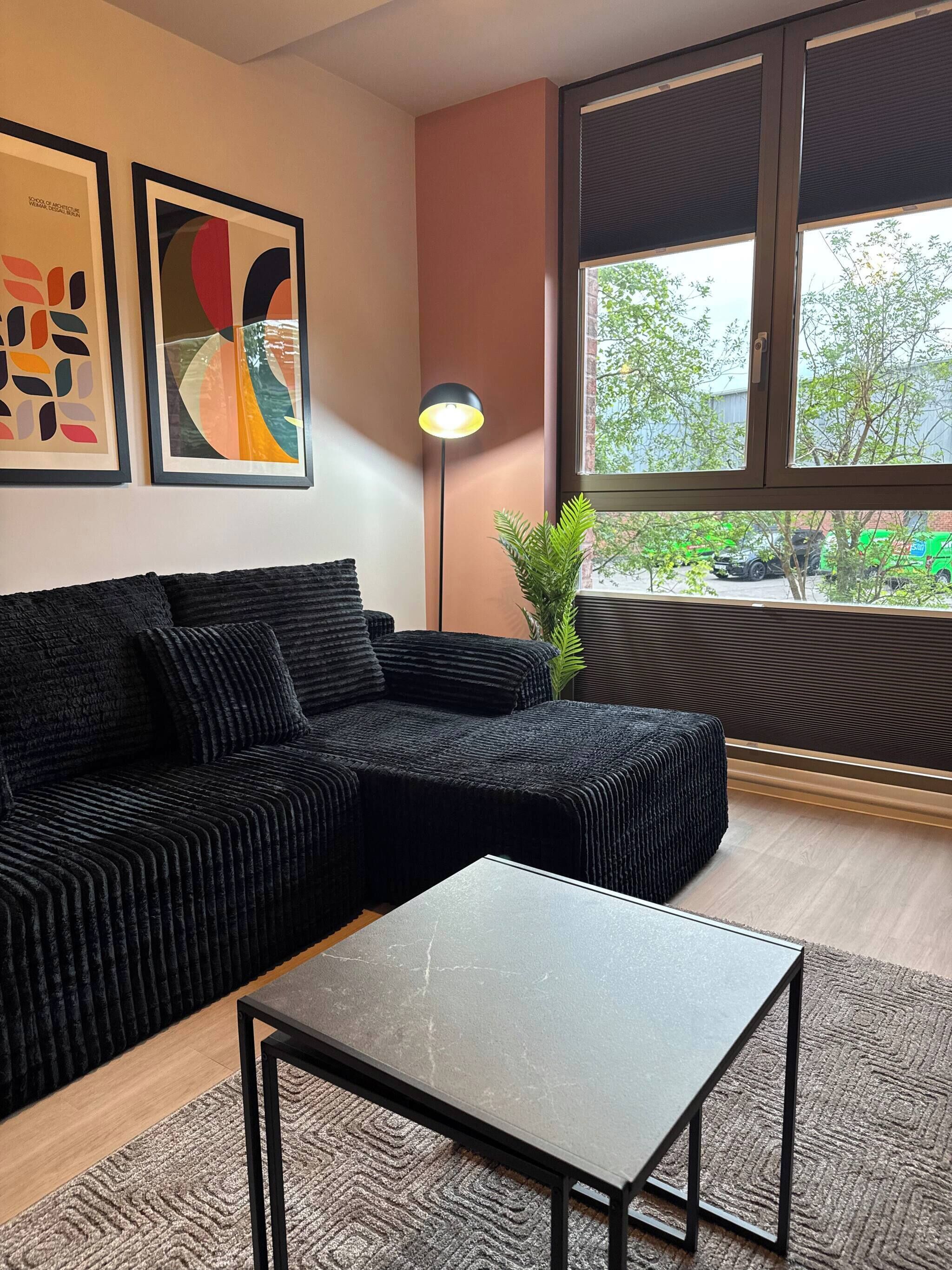 Una sala moderna con un sofá modular, una mesita y un ventanal con persianas.