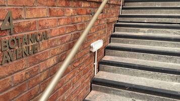 Een bakstenen muur met de tekst '4 BOTANICAL AVENUE' en een metalen leuning die naar een reeks betonnen trappen leidt.
