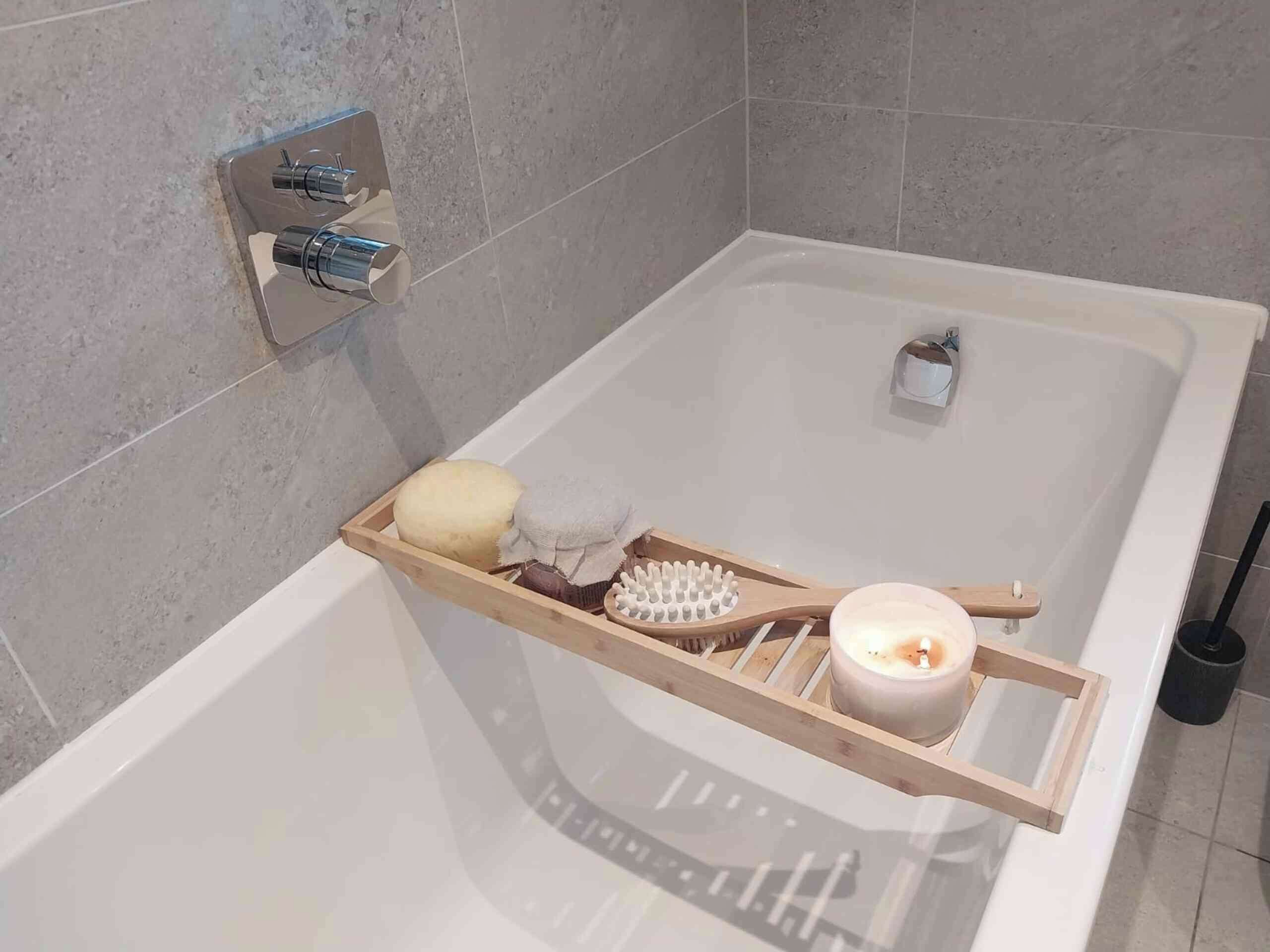 A bathroom with a bathtub, a wooden tray holding a candle, a brush, and a soap bar.