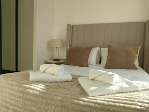 A neatly made bed with a beige headboard, a bedside table with a lamp, and two rolled towels on the bed. - 2 Bedroom 2 Bathroom Designer Apt Free Parking Finchley Central (London)