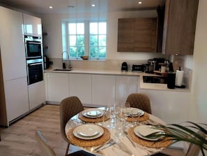 A modern kitchen with built-in appliances, a dining area with a table set for four, and a window providing natural light. - 2 Bedroom 2 Bathroom Designer Apt Free Parking Finchley Central (London)