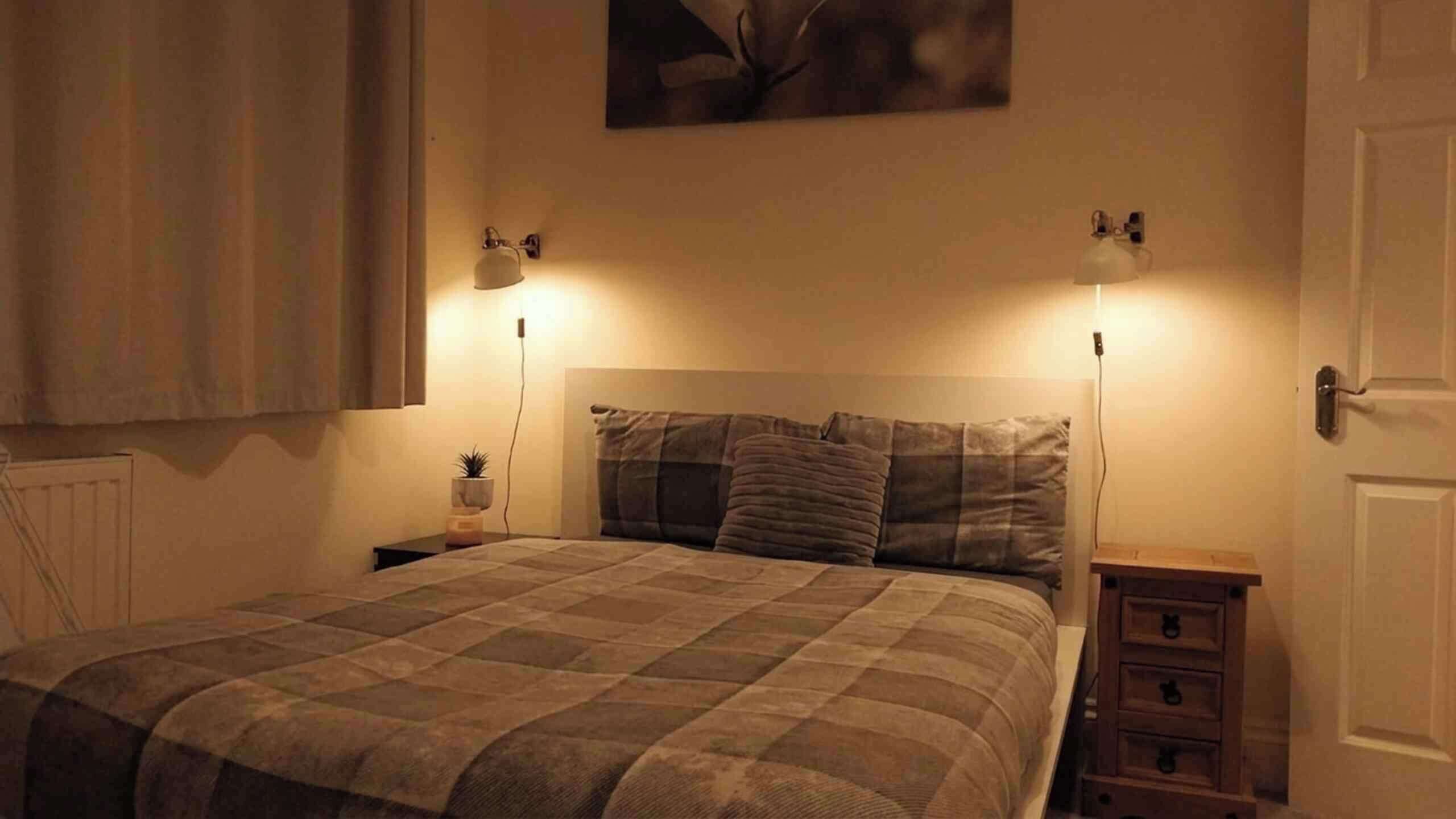 A bedroom with a bed, bedside tables, and wall-mounted lamps.
