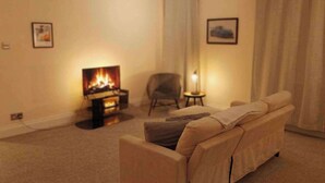 A living room with a sofa, a small table, a chair, a fireplace, and two framed pictures on the wall. - 1BR Apartment in Chislehurst High Street Sleeps 3 (Chislehurst)