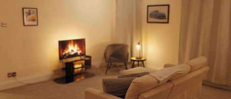 Una sala de estar con un sofá, una mesita, una silla, una chimenea y dos cuadros en la pared.