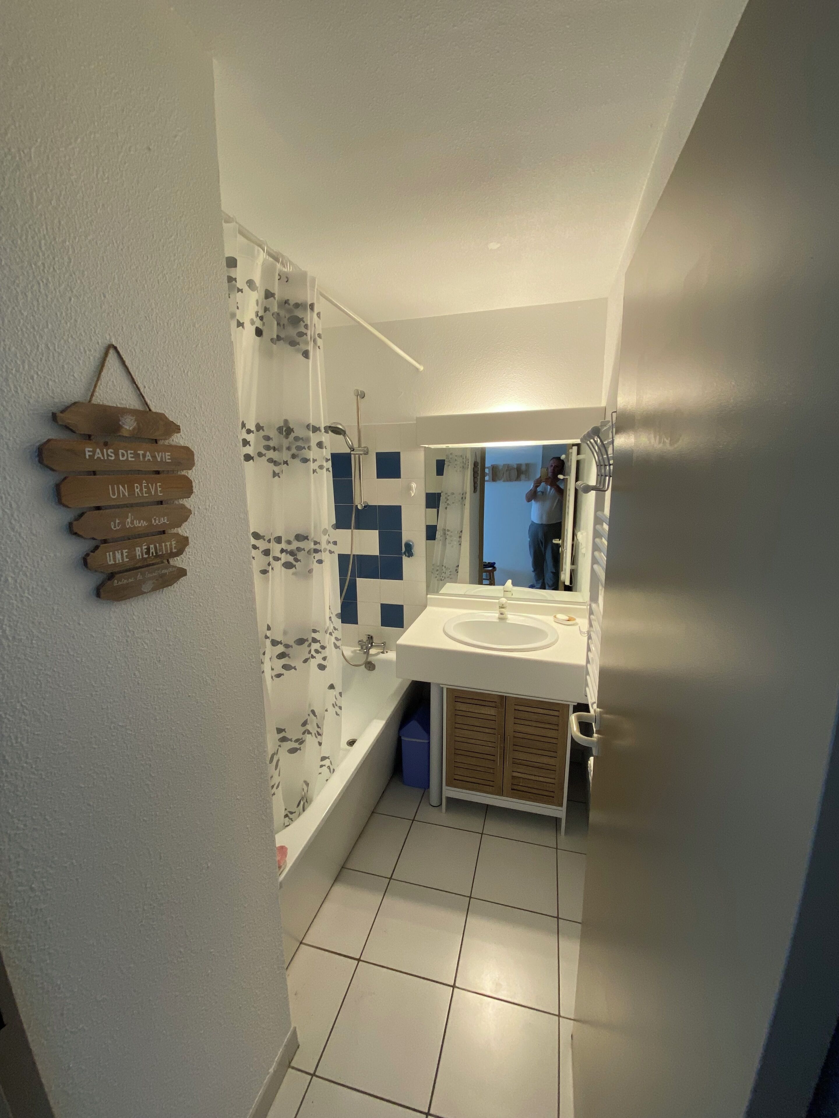 Ein Badezimmer mit Badewanne, Dusche und Waschbecken. An der Wand hängt ein Holzschild und über dem Waschbecken befindet sich ein Spiegel.