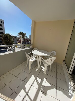 Ein Balkon mit weißem Tisch und Stühlen, gefliestem Boden und Blick auf Gebäude und Palmen.