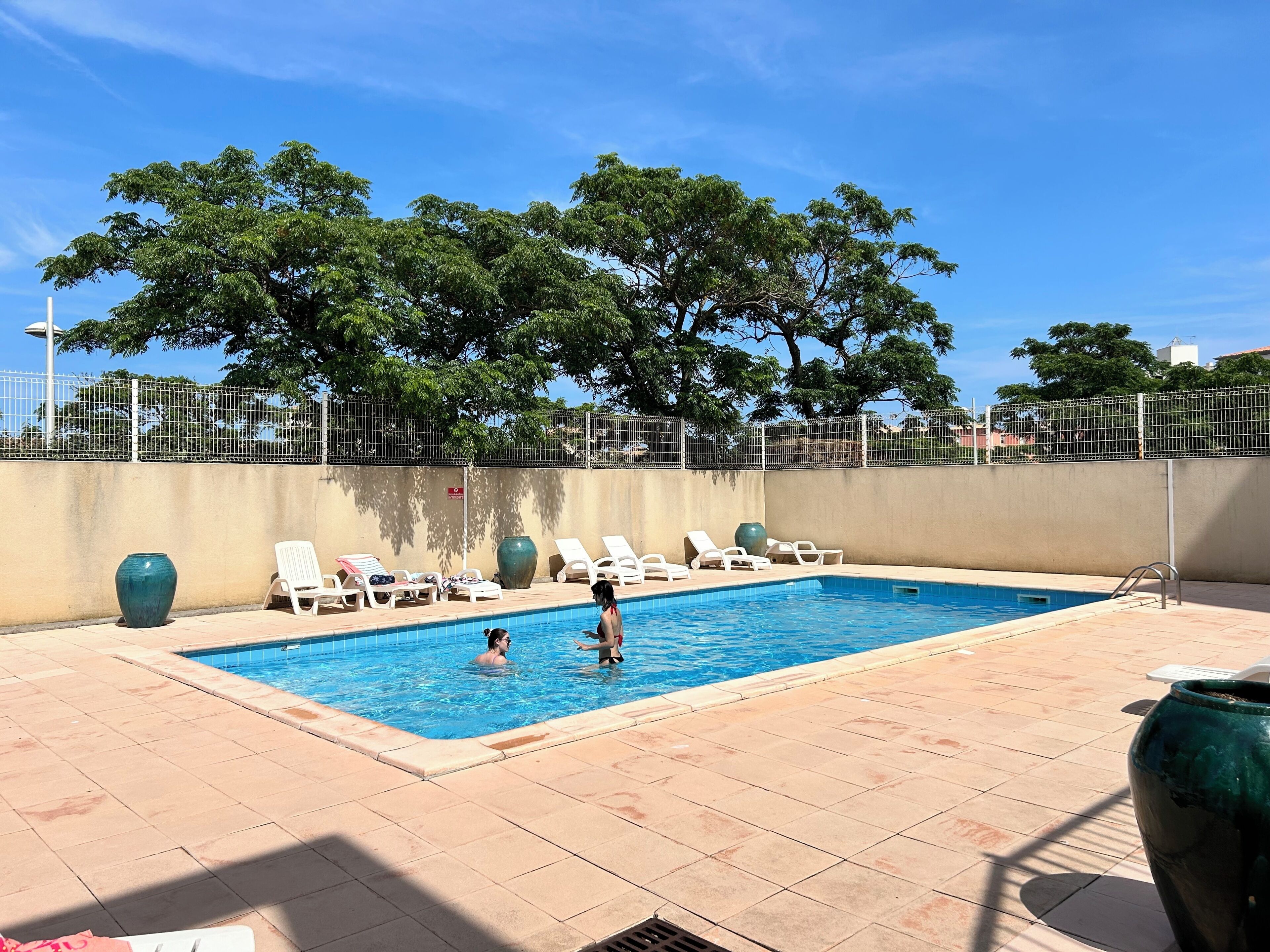 A swimming pool with lounge chairs and a tiled deck.