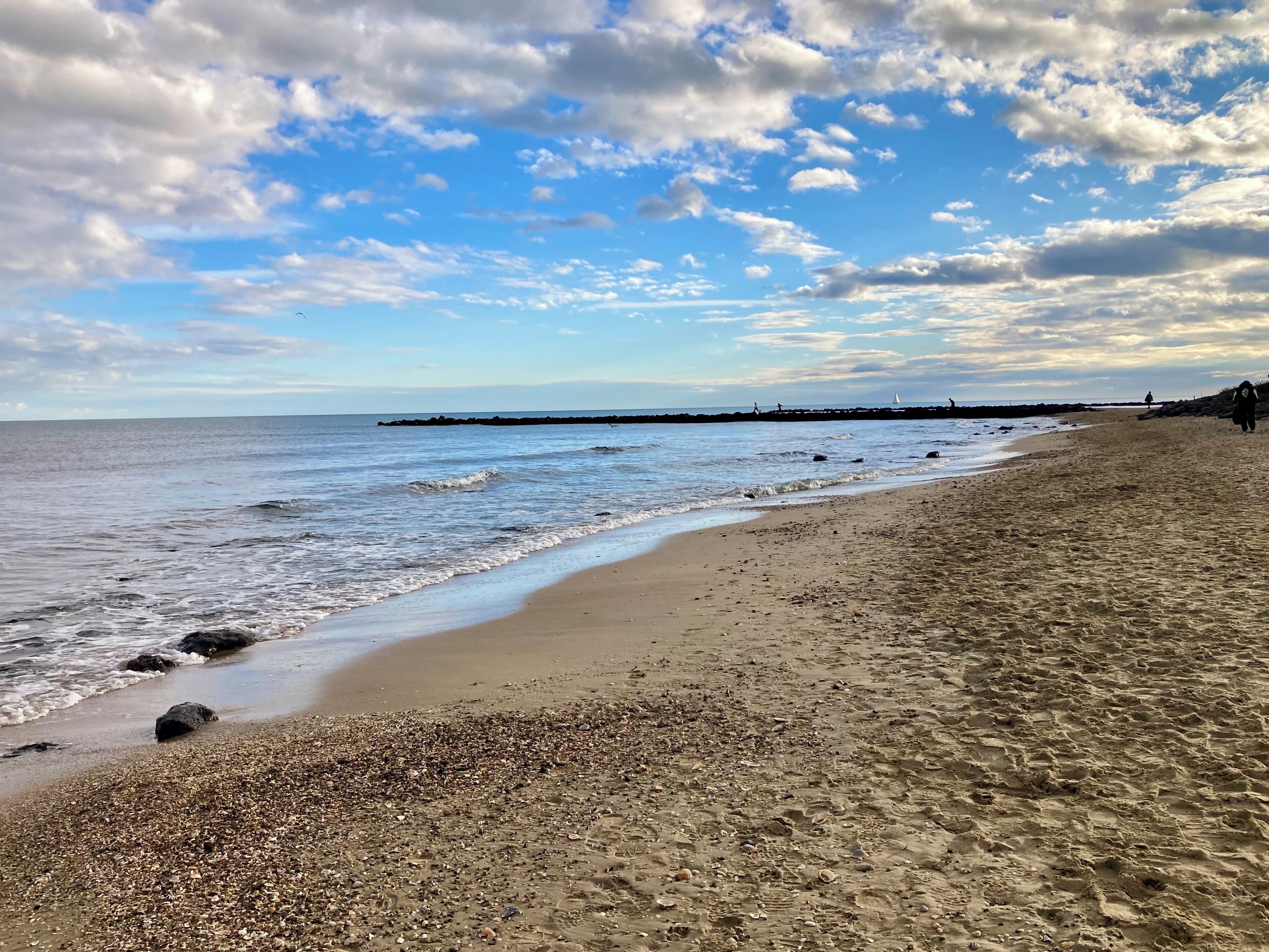 A beach with a pebbly shore, a distant jetty, and a clear sky.