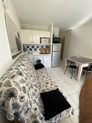 Ein kompakter Wohnraum mit Küchenzeile, Essbereich und Sofa mit blattbedecktem Bezug.