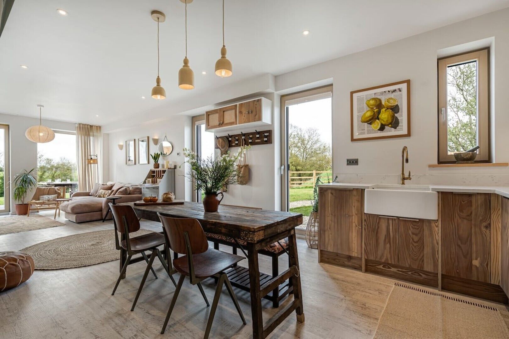 Cocina moderna con armarios de madera, una isla central, iluminación colgante y un gran ventanal que proporciona luz natural.