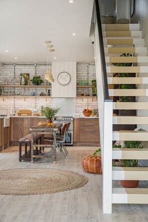 A modern kitchen with a wooden dining table, hanging pendant lights, and a staircase with a railing. - The Fold | A Tucked-Away 2 Bedroom Retreat In Buckinghamshire (Milton Keynes)