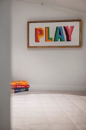 Una palabra enmarcada que dice 'PLAY' en una pared, con una pila de libros sobre una superficie blanca.
