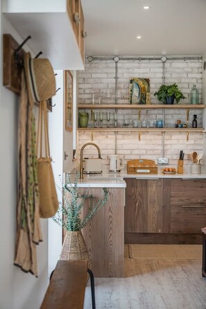 A kitchen with wooden cabinets, a white countertop, and hanging utensils. - The Fold | A Tucked-Away 2 Bedroom Retreat In Buckinghamshire (Milton Keynes)