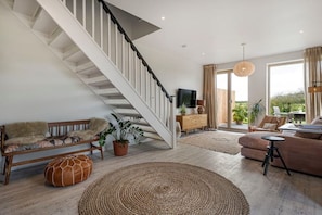A modern living room with a staircase, a sofa, a coffee table, and a view of the outdoors. - The Fold | A Tucked-Away 2 Bedroom Retreat In Buckinghamshire (Milton Keynes)