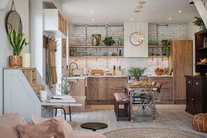 A modern kitchen with a brick wall backsplash, wooden cabinets, and a dining area with a rustic table and chairs. - The Fold | A Tucked-Away 2 Bedroom Retreat In Buckinghamshire (Milton Keynes)