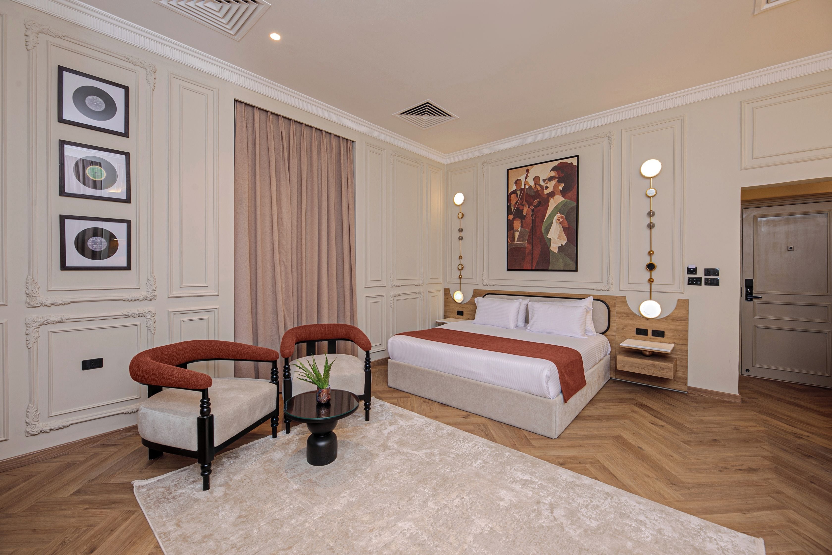 Une chambre d’hôtel avec un lit, deux chaises, une petite table, un tableau et une porte.
