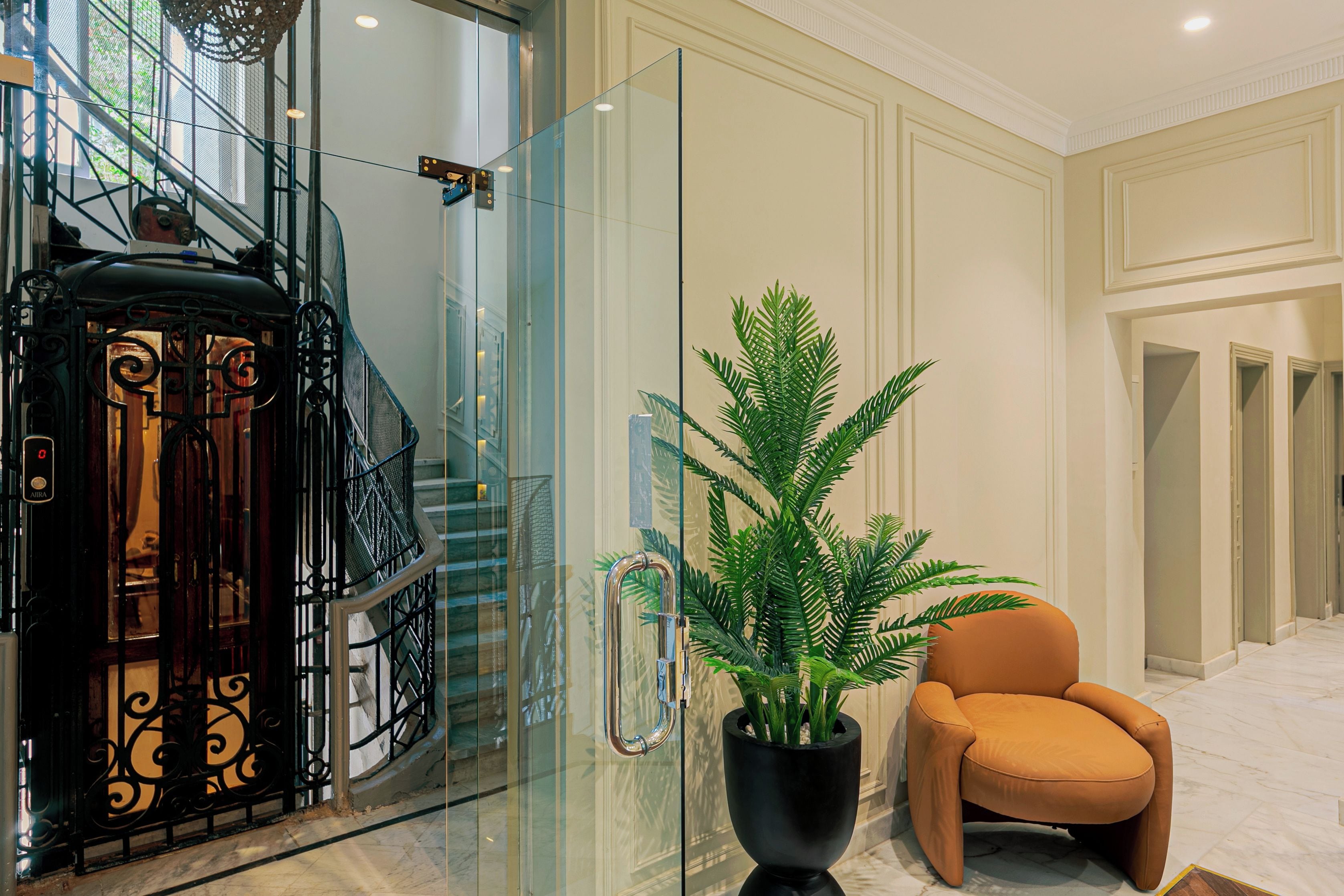 Un interior moderno con un ascensor de vidrio, una planta en maceta y un sillón de cuero.