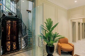 Un interior moderno con un ascensor de vidrio, una planta en maceta y un sillón de cuero.