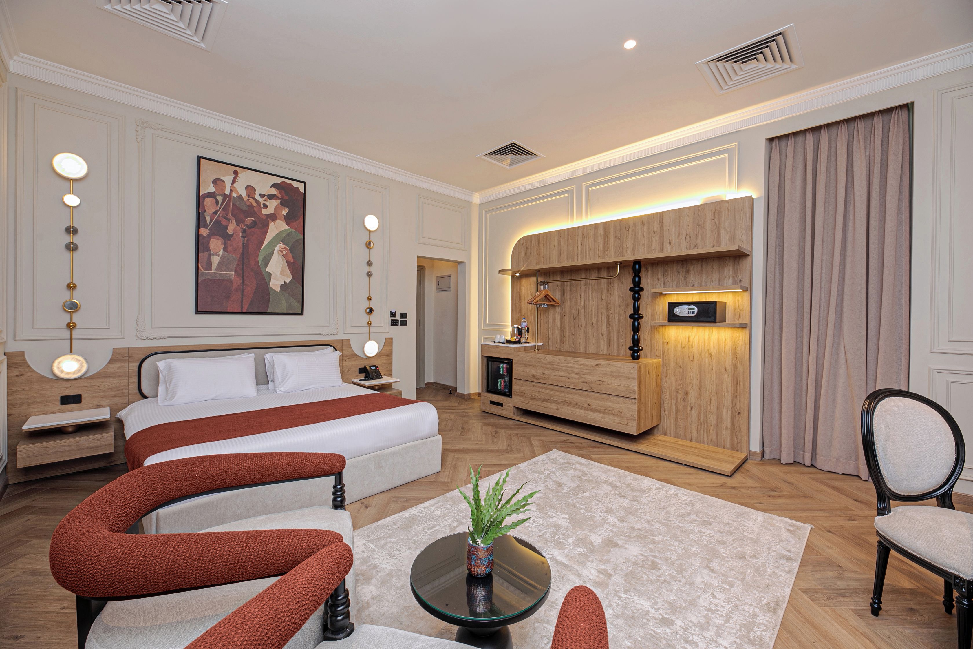 A hotel room with a large bed, a desk, a seating area with a table and chairs, a painting on the wall, and a wooden cabinet with a built-in microwave.