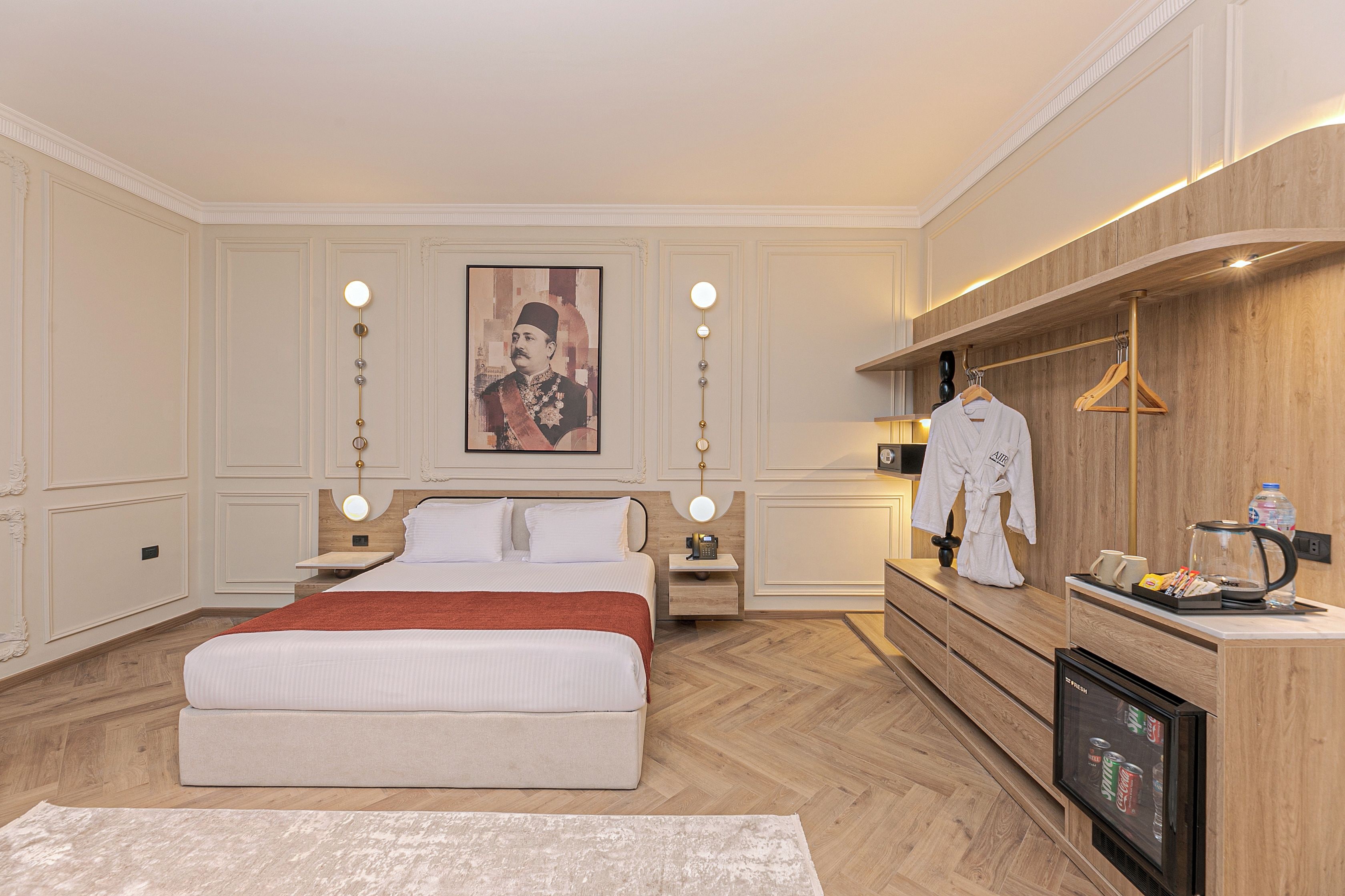 A hotel room with a large bed, a vanity with a mirror, a robe hanging, a coffee machine, and a minibar.