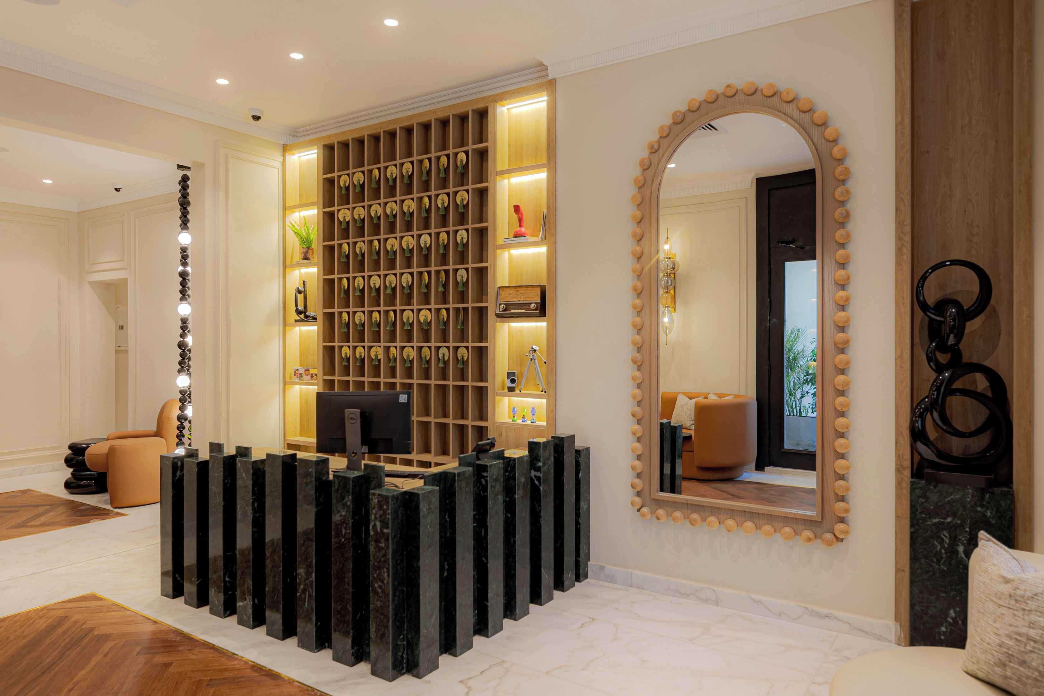 A reception area with a marble floor, a reception desk, a wall-mounted mirror, and a wooden panel with framed items.