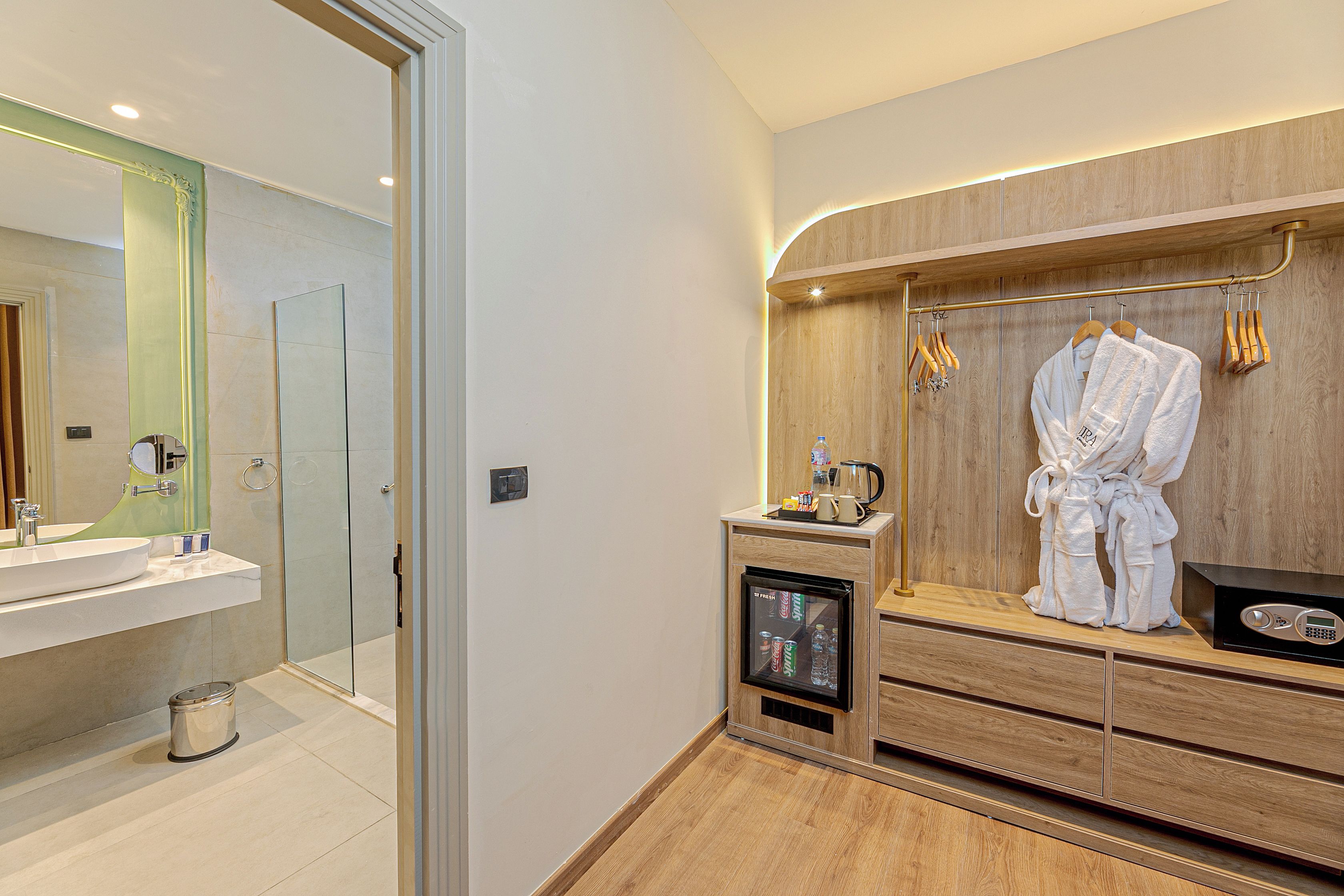 Ein modernes Badezimmer mit einer Glasdusche, einem Waschtisch mit Spiegel und einem Holzwäschetisch, an dem ein Bademantel hängt.
