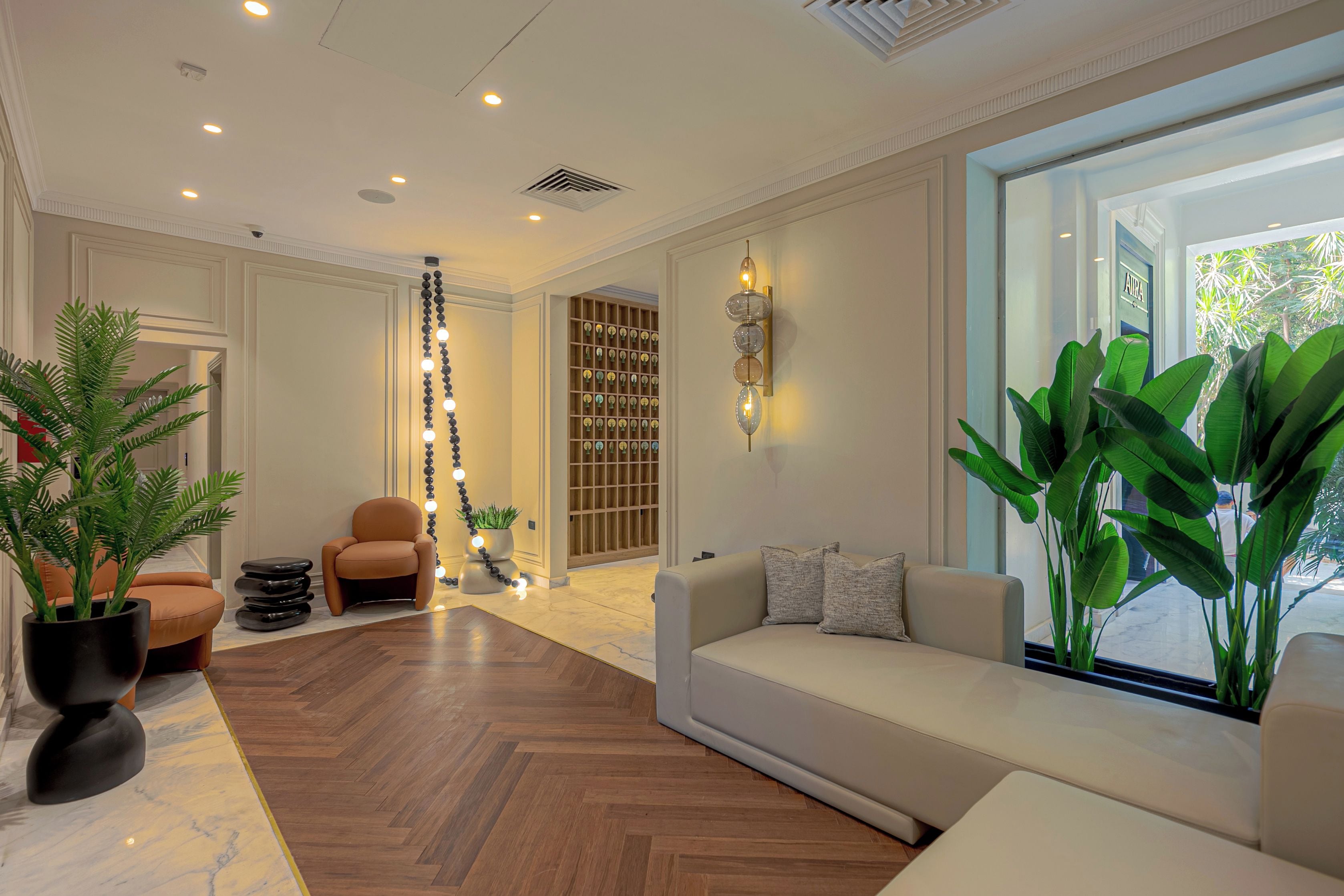 Een moderne woonkamer met een bank, een salontafel, een kamerplant, een wandlamp en een groot raam.