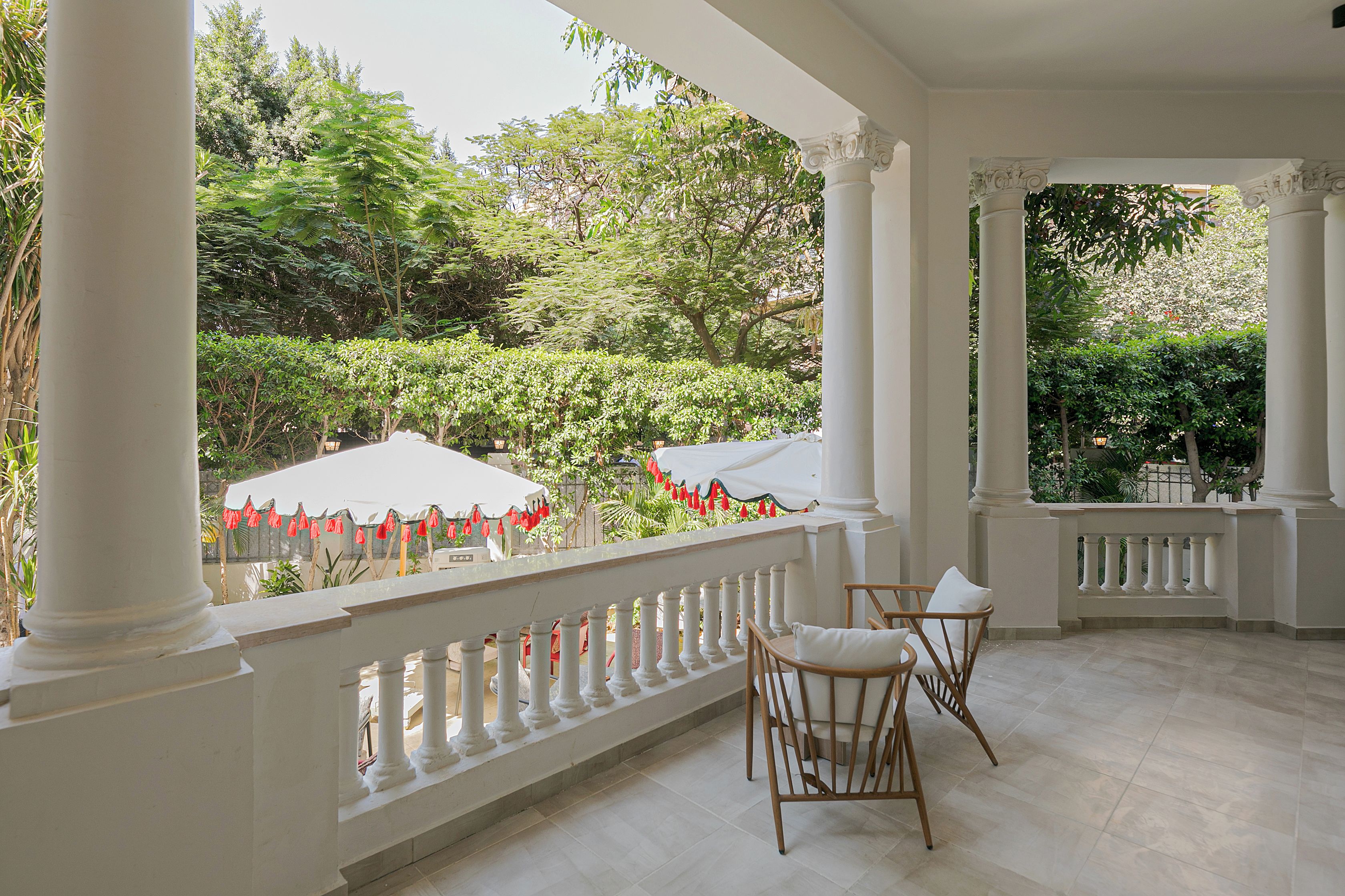 A covered outdoor area with white columns, a white railing, and two wicker chairs with white cushions.