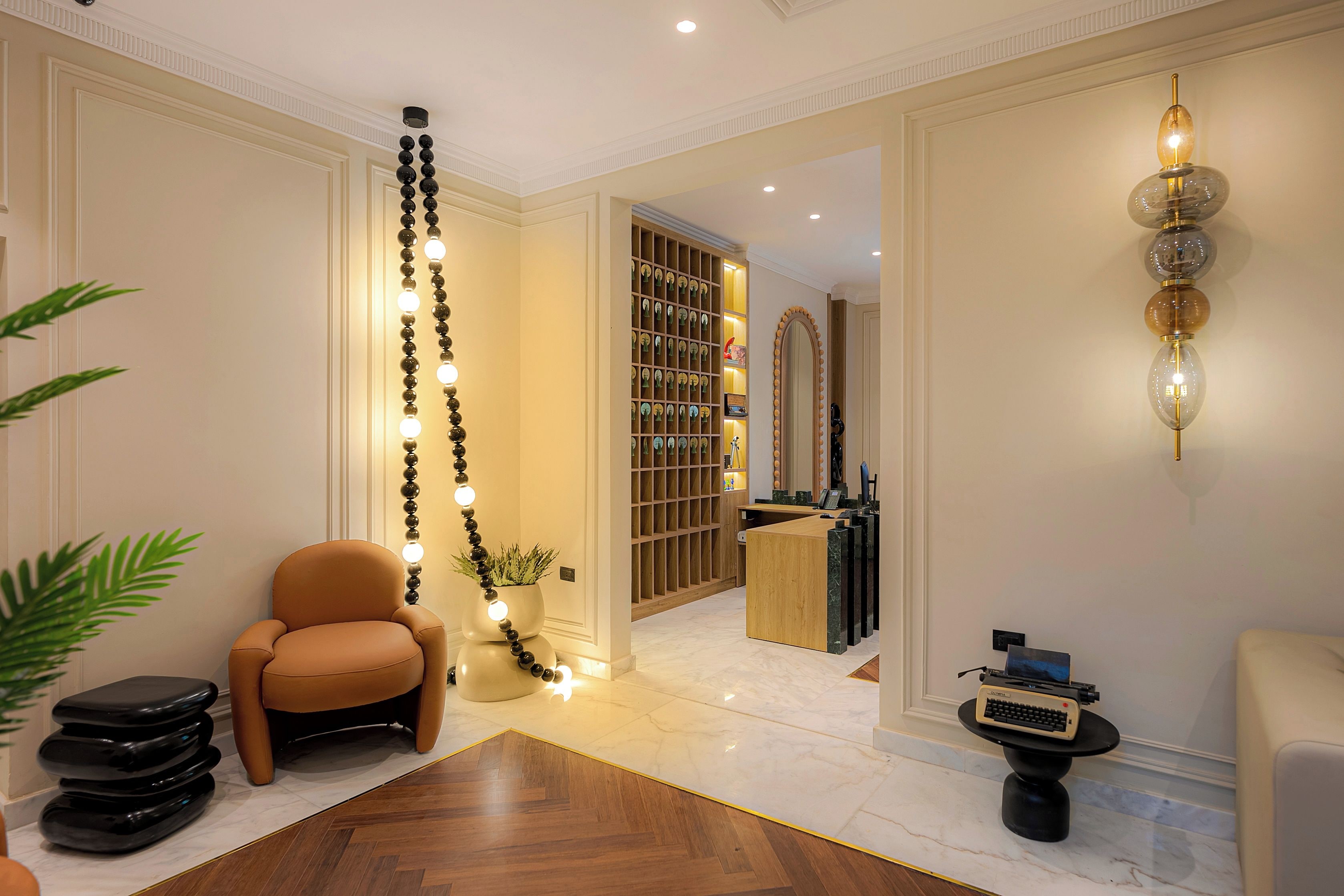 A hotel lobby with a reception desk, a seating area with a chair, a decorative wall with lights, and a plant.