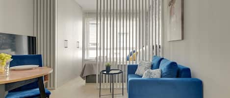 A modern living space with a blue sofa, a round wooden table with chairs, and a small side table with a plant.