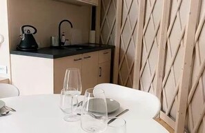 A dining area with a table set for two, a kitchen in the background, and a patterned wall. - Restart Kaszuby - Jurta w sercu Kaszub (Dejk)