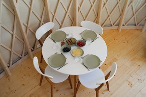 A round table with six white chairs, set for a meal with plates, cutlery, and a bowl of berries. - Restart Kashubia - Yurt in a Landscape Park (Dejk)