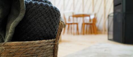 Un panier en osier contenant un objet sombre, une table et des chaises en bois en arrière-plan, et un objet noir sur la droite.