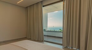 Ein Hotelzimmer mit einem großen Bett, einer Schiebetür zu einem Balkon mit Meerblick.