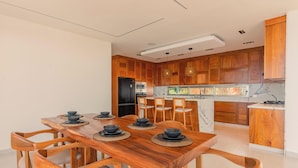 A modern kitchen with wooden cabinets, a dining table with chairs, and a built-in oven. - Villa Rose (Las Terrenas)
