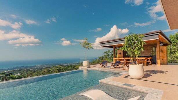 A modern outdoor pool area with a clear view of the ocean and a wooden building with a dining area. - Villa Rose (Las Terrenas)