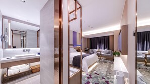 Een moderne hotelkamer met een groot bed, een slaapbank, een klein tafeltje, een badkamer met een wastafel en spiegel, en een grote spiegel.