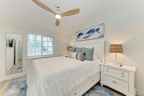 A bedroom with a bed, a nightstand, a ceiling fan, a window, and a painting on the wall. - The Blue Haven: Ground level 2 BR with private pool! (Holmes Beach)