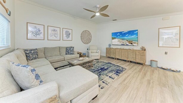 Ein Wohnzimmer mit Ecksofa, Couchtisch, Beistelltisch, Schrank, Teppich und Deckenventilator.