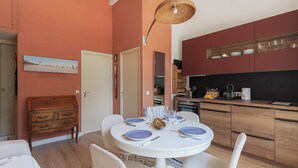 A dining area with a round table, white chairs, and a ceiling light fixture. - Flat in a Traditional Norman Townhouse - Garden (Deauville)