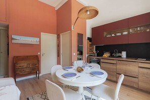 A dining area with a round table, white chairs, and a ceiling light fixture. - Flat in a Traditional Norman Townhouse - Garden (Deauville)