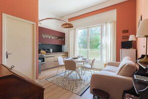 A modern kitchen with a dining area, a sofa, and a TV. - Flat in a Traditional Norman Townhouse - Garden (Deauville)