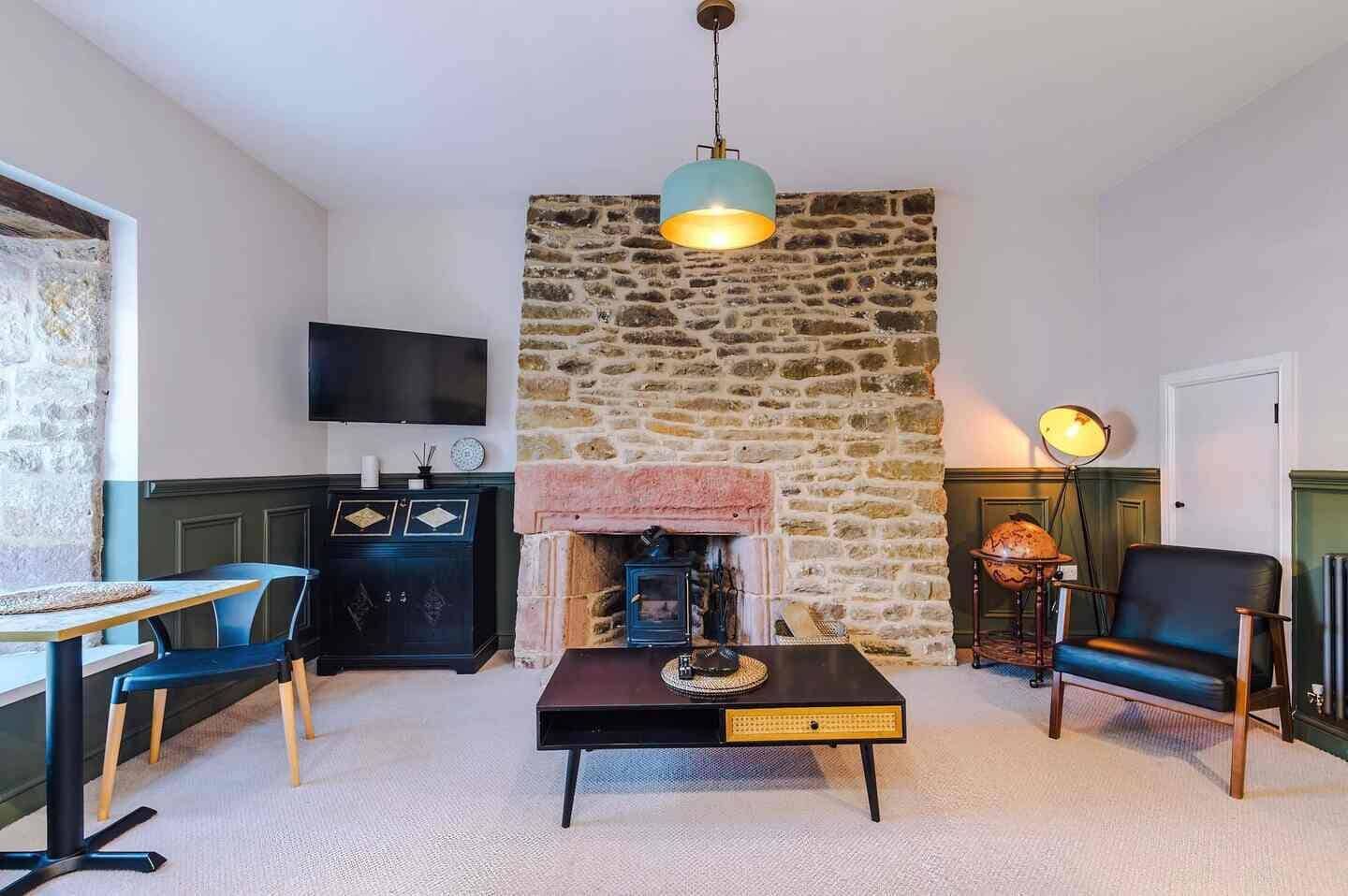 A cozy living room with a stone wall, a fireplace, a television, and a dining area with chairs and a table.
