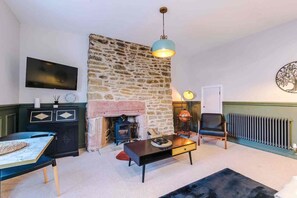 Una sala de estar con pared de piedra, chimenea, televisor y una lámpara colgante azul.