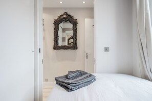 A bedroom with a bed, a folded towel, a mirror, and a door. - Elegant Chelsea Apartment | 2 Bedrooms | Prime Zone 1 Location (London)
