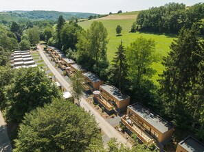 Ein modernes Hotel mit mehreren Gästezimmern, die entlang einer Straße angeordnet sind, umgeben von üppiger Vegetation und Hügeln im Hintergrund.