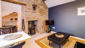 A room with a stone wall, a fireplace, a television, and a dining area with a table and chairs. - The Vault - Boutique Cosy Peak District Retreat in a Grade II listed building (Chapel-en-le-Frith)