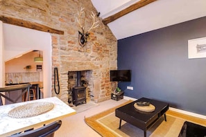A room with a stone wall, a fireplace, a television, and a dining area with a table and chairs. - The Vault - Boutique Cosy Peak District Retreat in a Grade II listed building (Chapel-en-le-Frith)